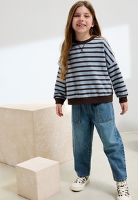 Jersey a rayas azul y marrón, ajuste relajado, combinado con vaqueros azules holgados y zapatillas blancas. Textura suave, diseño informal.