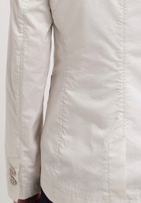 Jakk keva ringan bertekstur dengan desain yang pas, jahitan yang terlihat, dan aksen kancing di pergelangan tangan.