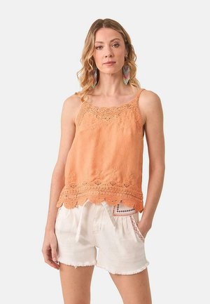 Top de tirantes de color melocotón con detalles de encaje en el escote y el dobladillo, combinado con pantalones cortos blancos deshilachados que presentan costuras decorativas.