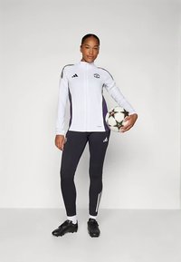 Jachetă sport albă cu accente mov și colanți negri, având trei dungi albe. Figura ține o minge de fotbal, purtând ghete negre.