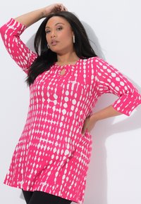 Różowa tunika w białe kropki, z okrągłym dekoltem z wycięciem typu keyhole oraz rękawami do łokcia. Miękka faktura tkaniny.