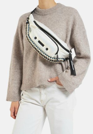 Witte gewatteerde schoudertas met gevlochten banddetail, zwarte rits en een klein zakje aan de voorkant. Het model draagt een beige trui en witte broek.
