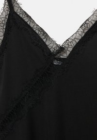 Fekete ruhadarab V-kivágással, finom csipke díszítéssel és rojtos szélekkel. A sima textúra kontrasztban áll az aprólékos csipke részletekkel.