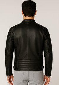 Uomo visto da dietro che indossa una giacca di pelle nera attillata con spalle imbottite e vita, abbinata a jeans grigio chiaro.