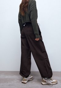 Honingkleurige cargobroek met zijzakken, gecombineerd met een donkergroen cropped kabeltrui en witte sneakers met beige accenten.