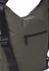 Bolsa de tela verde para el hombro con correa negra ajustable y dos bolsillos visibles con cremallera negra, uno horizontal en la parte delantera y otro inclinado en la parte superior.