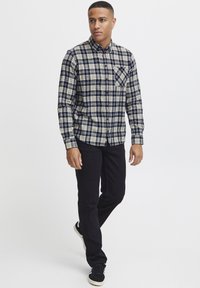 Rutete flanellskjorte i marineblå og krem, med krage med knapper, lange ermer og en frontlomme. Kombinert med svarte bukser og sneakers.