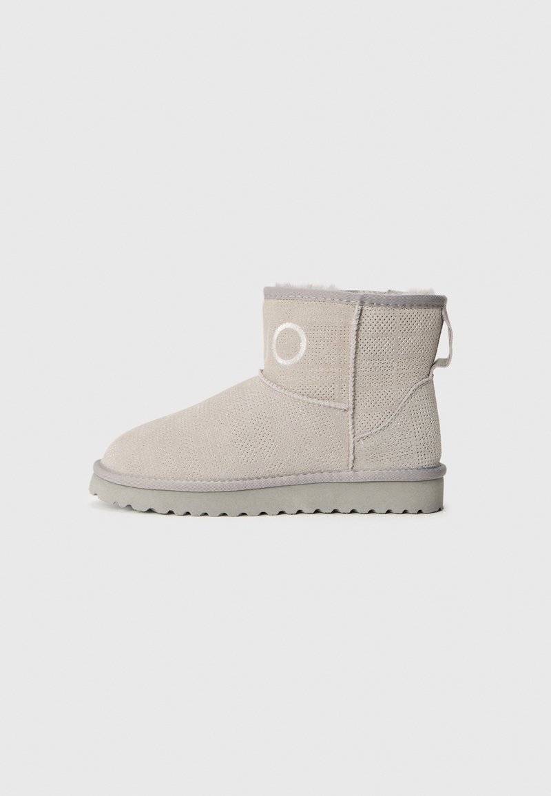 Bottines beige en tissu texturé avec un détail rond du logo, semelle grise et doublure douce, dotées d'une boucle à l'arrière.