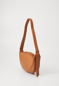 Bolso de hombro de cuero marrón claro con forma redondeada, correa ajustable y cierre superior de cremallera. Textura suave con acentos mínimos.