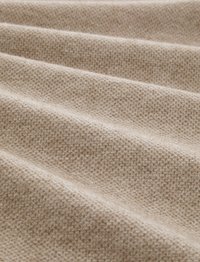 Tissu beige texturé avec un motif tissé, présentant des crêtes douces et surélevées ainsi qu'une apparence lisse et chaleureuse dans une position drapée.