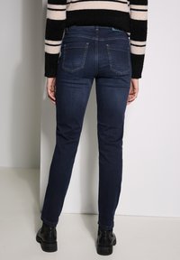 Jeans ajustados de color azul oscuro con una textura suave, diseño de cinco bolsillos y costuras en contraste. Llevados con botines negros.