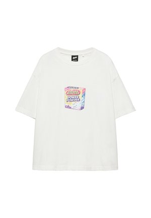Junger Mann steht, trägt ein weißes T-Shirt mit buntem Grafikmotiv und grüne karierte Shorts mit dem Text "City", graue Sneakers und eine Perlenkette.