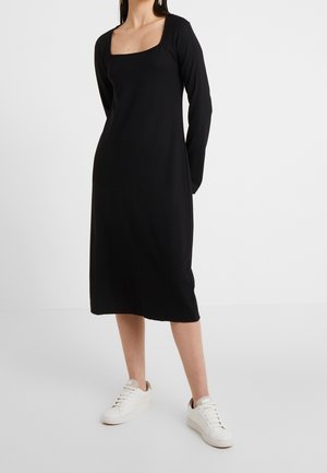 Czarna sukienka na długi rękaw z kwadratowym dekoltem, wykonana z gładkiej tkaniny o luźnym kroju. W zestawieniu z białymi sneakersami dla casualowego wyglądu.