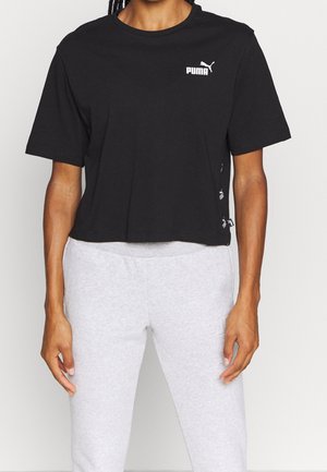Osoba nosząca czarny krótki T-shirt Puma i jasnoszare spodnie dresowe na jednolitym tle.