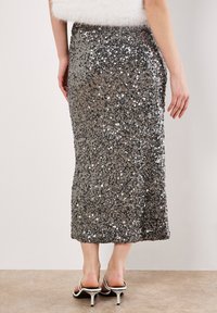 Gonna midi in paillettes nei toni argento e grigio, con vita aderente, texture liscia e silhouette dritta, abbinata a tacchi aperti.