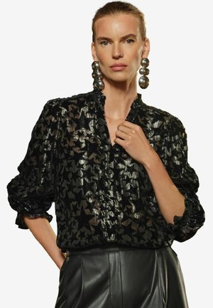 Bluză cu model de stele negre, cu un finisaj texturat, închidere cu nasturi și guler cu volane. Asortată cu cercei mari din argint lucios.