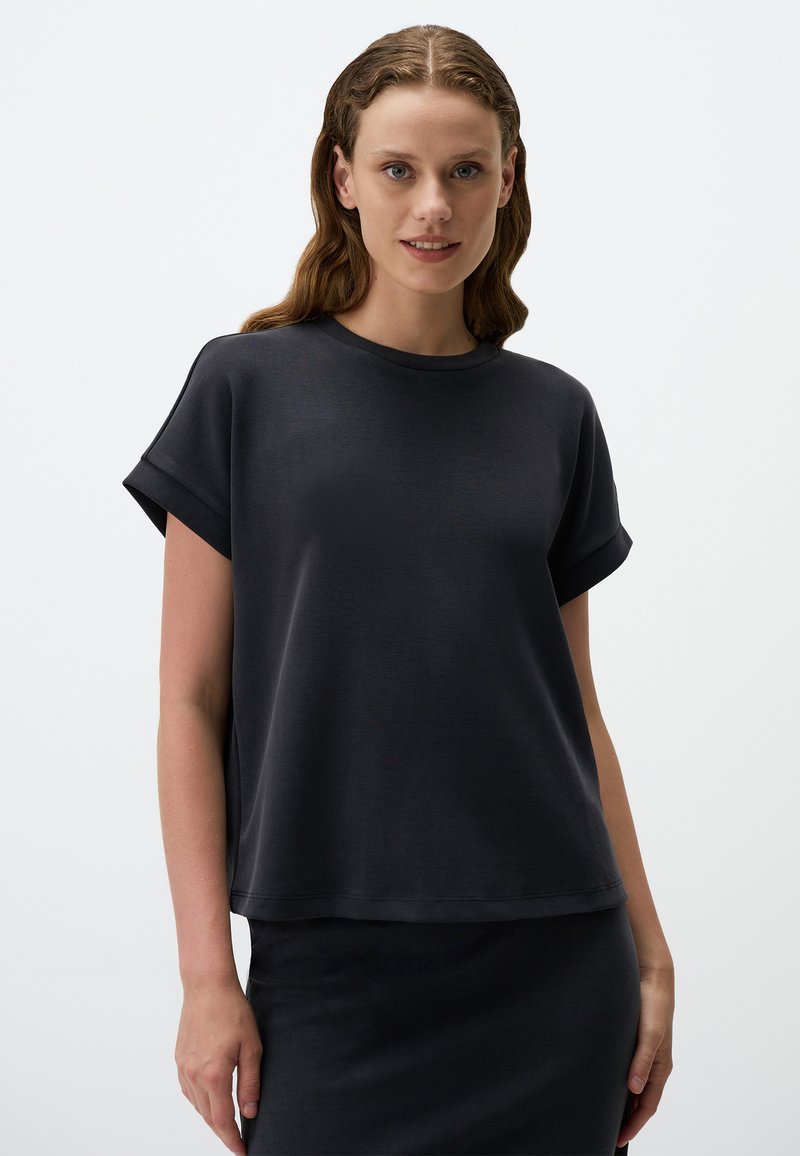 Czarna koszulka z krótkim rękawem, okrągłym dekoltem, luźnym krojem, gładką teksturą i podwiniętymi mankietami, w zestawie z dopasowaną czarną spódnicą.