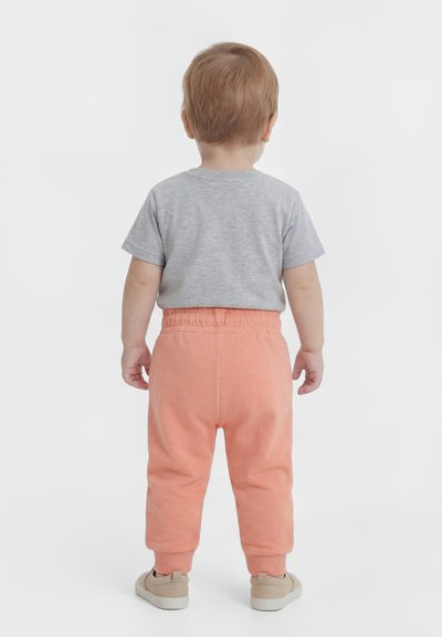Νήπιο που στέκεται με την πλάτη προς το αντικείμενο, φορά γκρι μπλούζα κοντού μανικιού, κοραλί παντελόνι με ελαστική μέση και ανοιχτό μπεζ παπούτσια σε λευκό φόντο.