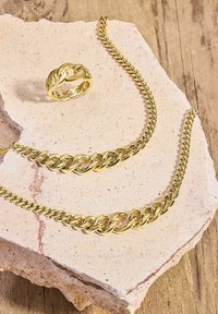 Conjunto de collar y anillo de cadena de oro con eslabones entrelazados, acabado pulido, exhibido sobre una piedra texturizada. Los acentos incluyen un diseño minimalista.