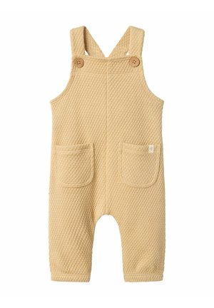 Beige Strickoveralls mit einem strukturierten Muster, ausgestattet mit zwei vorderen Taschen und Holzknöpfen an verstellbaren Trägern.