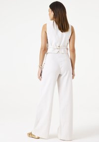 Lichtgekleurde linnen vest met een getailleerde taille en gespsluiting, gecombineerd met brede, off-white broek; gladde textuur, minimalistisch ontwerp.