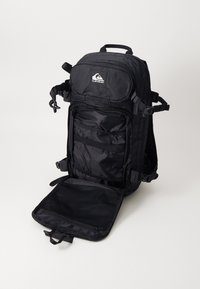 Black backpack with adjustable straps, multiple compartments, and a front zip pocket. It features a smooth fabric and a mesh section inside.