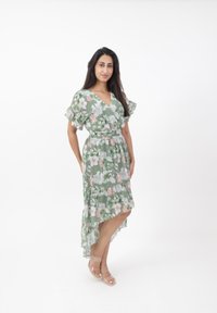 Vestito avvolgente floreale verde, con maniche corte a volant, orlo asimmetrico e cintura con fiocco. Adornato con fiori rosa e bianchi.
