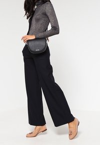 Czarna torebka na ramię o teksturowanej powierzchni, zestawiona z ciemnym golfem i czarnymi, szerokimi spodniami. Jasnobrązowe mokasyny z dekoracyjnymi detalami.