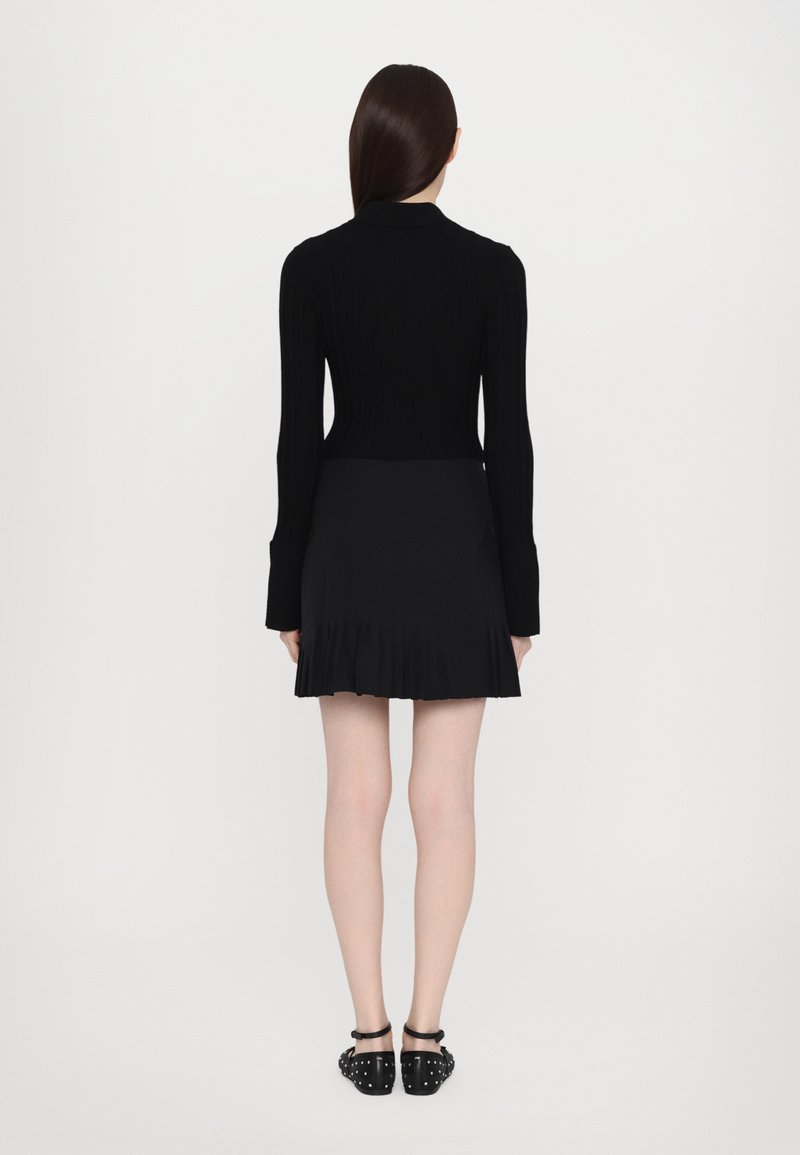 Maglione nero a coste con maniche lunghe, abbinato a una gonna plissettata nera. L'outfit presenta un design aderente e scarpe nere flat con borchie.