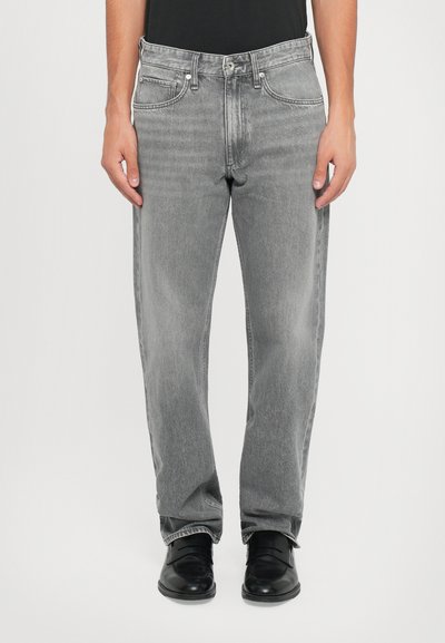 Grå denim jeans med lige pasform, der har fem lommer, knaplukning og let slid. Bæres med sorte sko.
