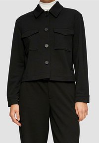 Sort cropet jakke med krave, knapper foran og to brystlommer, lavet af et glat stof i en ensfarvet nuance.