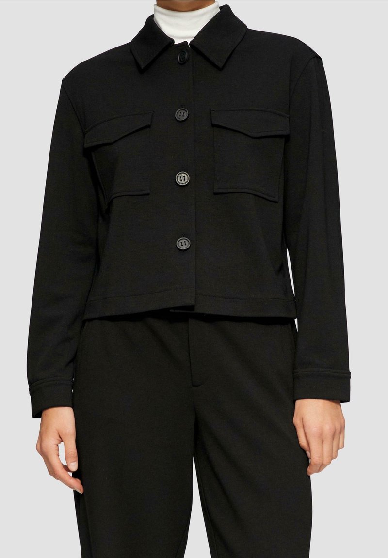 Sort cropet jakke med krave, knapper foran og to brystlommer, lavet af et glat stof i en ensfarvet nuance.