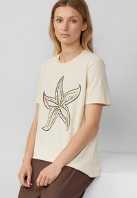 Cream-colored short-sleeve T-shirt featuring a large starfish graphic in black, red, yellow, and blue, made from soft cotton material.