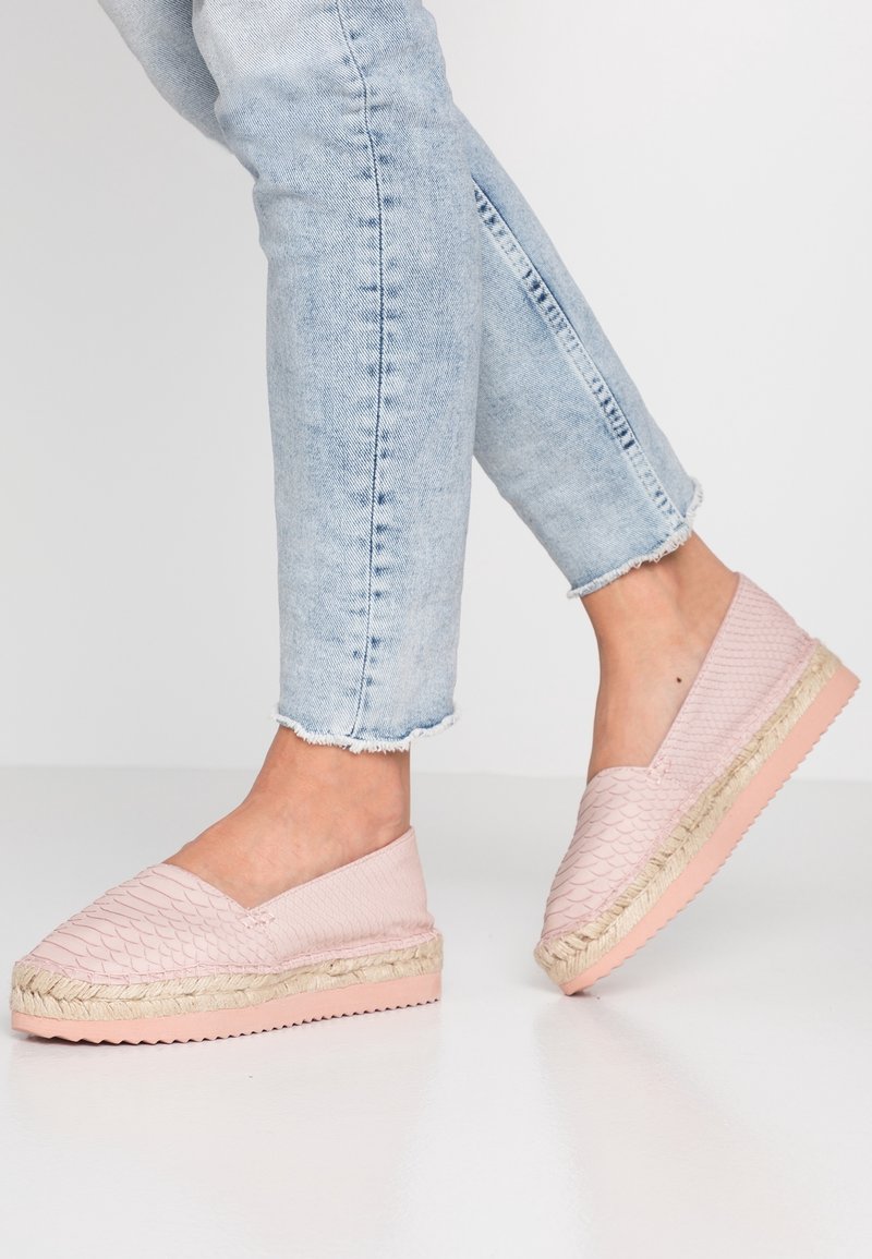 Espadrilles roses pâles à enfiler avec une texture matelassée, une semelle intermédiaire en corde de jute et une semelle extérieure en caoutchouc, portées avec un jean bleu clair retroussé.