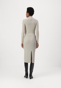 Brei trui met hoge hals, lichtgrijze kleur. Geribbelde textuur, aansluitende silhouet. Gecombineerd met lange geribbelde rok met een split aan de achterkant. Zwarte laarzen tot de knie.