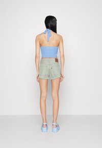 Top de ganchillo azul, pantalones cortos de mezclilla verde menta con dobladillo deshilachado, parche de marca marrón en los pantalones cortos, combinados con zuecos azul claro.