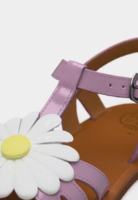 Μωβ παιδικό σανδάλι με μεγάλη λευκή και κίτρινη διακόσμηση μαργαρίτας και ασημένιο λουράκι με αγκράφα σε καφέ σόλα.