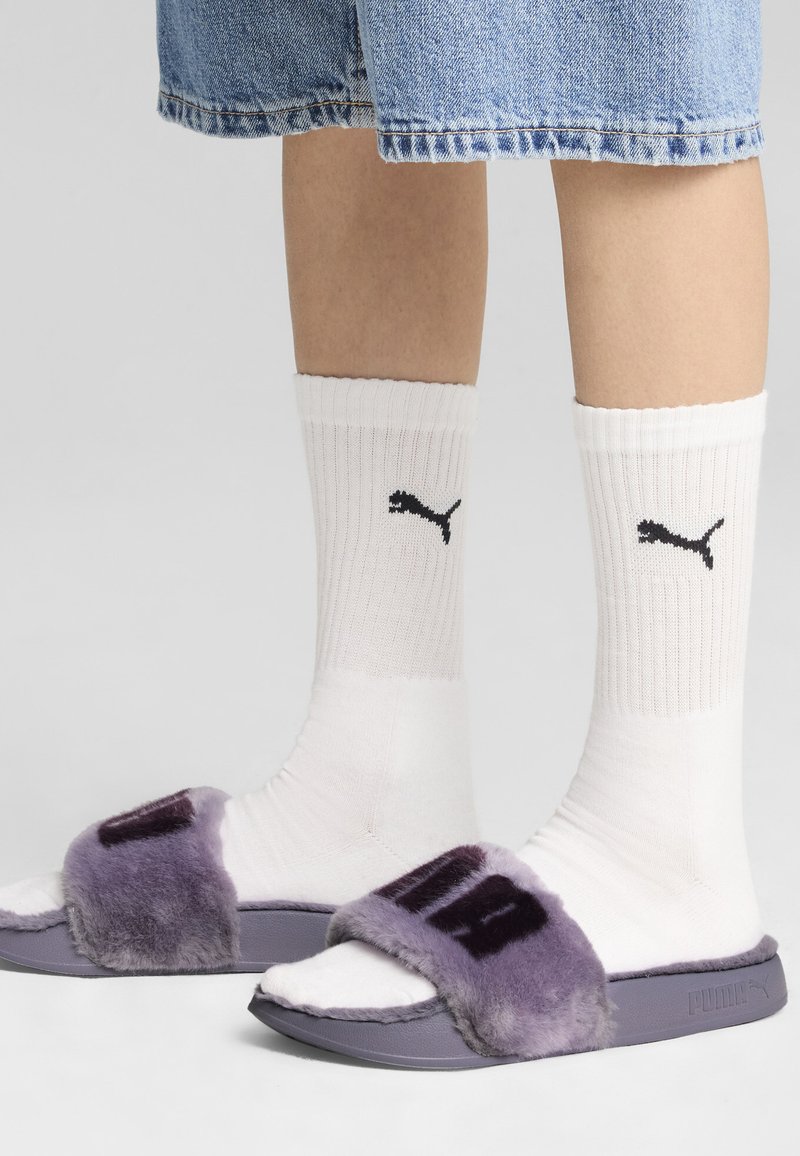 Fioletowe futrzane klapki na płaskiej białej podeszwie, z szerokim paskiem i logo "PUMA" w ciemnofioletowym kolorze. W zestawie z białymi skarpetkami w prążki.