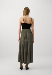 Jupe maxi tiered vert foncé avec une silhouette fluide, associée à un top en tank noir ajusté, mettant en valeur des bretelles fines et un design simple.