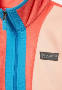 Kurtka polarowa Columbia z jasnoczerwonym korpusem, niebieskim zamkiem i szarym logo. Miękka tekstura, z zapięciem na zamek i kapturem.