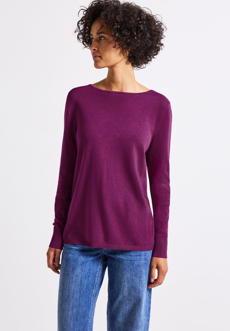 Lila langärmliger Pullover mit weitem Ausschnitt und gerippten Bündchen, aus einem weichen, leichten Material, kombiniert mit blauen Jeans.