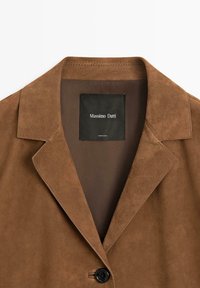Bruine suède blazer met inkeping revers, enkele zwarte knoopsluiting en zichtbare "Massimo Dutti" label aan de binnenkant van de kraag.