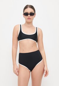 Juodas bikinis su baltais akcentais, savyje turintis kvadratinį iškirpimą ir aukšto liemens apatinius. Pagamintas iš sklandžios medžiagos, su prigulniu dizainu.