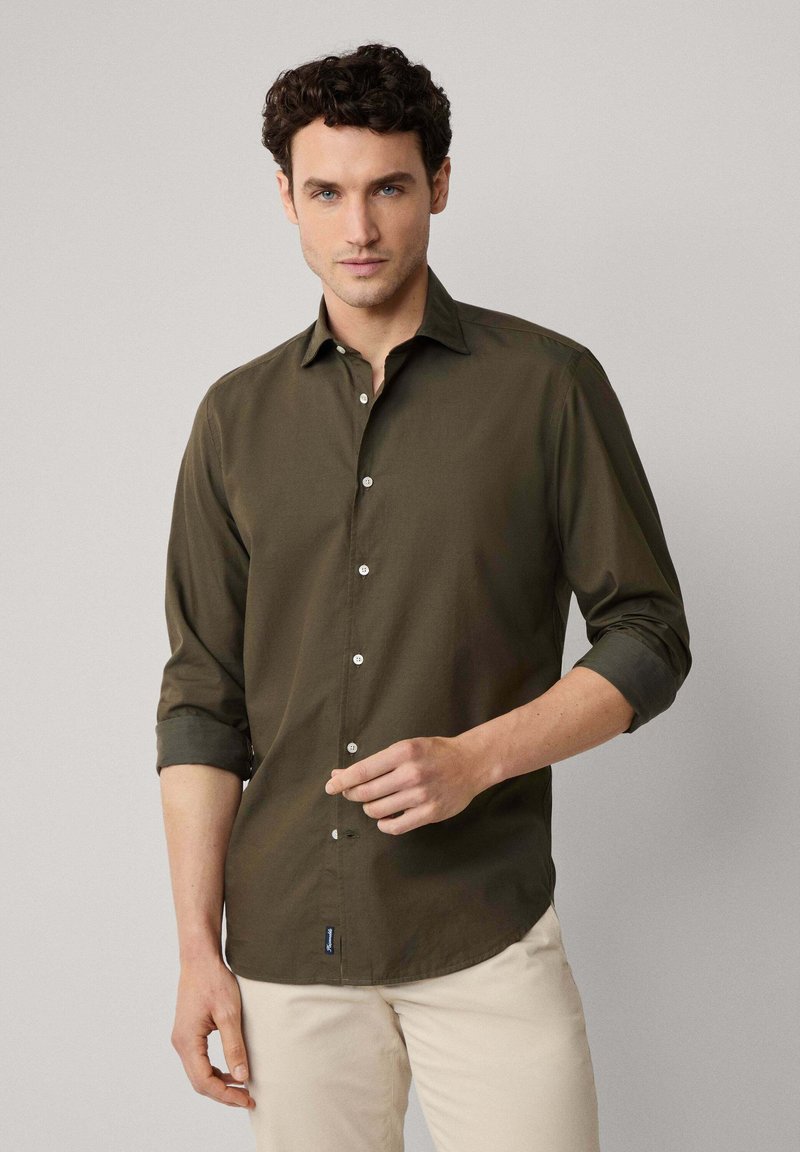 Camisa de botones en verde olivo oscuro con cuello, mangas enrolladas y botones blancos. Tela suave con una textura lisa y una etiqueta de marca sutil.