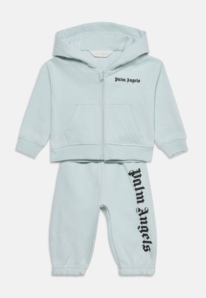 Survêtement bleu clair pour tout-petit avec sweat à capuche zippé et pantalon avec texte noir "Palm Angels" sur la poitrine et la jambe du pantalon.