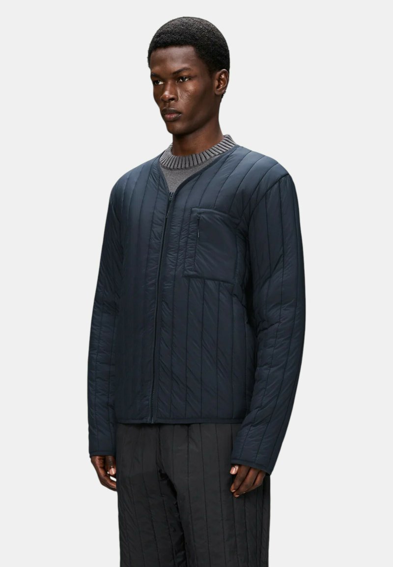 Mørkeblå quiltet jakke med lodrette striber, har lynlåslukning og en patchlomme på venstre bryst. Lavet af letvægtsstof.