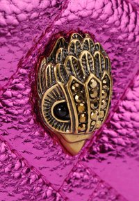 Metallic różowa torebka z teksturowanej powierzchni, ozdobiona zapięciem w złotym odcieniu przypominającym stylizowaną twarz i zdobiona cyrkoniami.