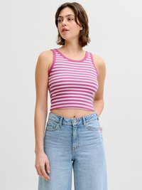 Γυναίκα με ροζ-λευκό ριγέ μπουστάκι χωρίς μανίκια, συνδυασμένο με ψηλόμεσο τζιν ανοιχτού μπλε χρώματος, που στ έκεται μπροστά σε απλό φόντο.