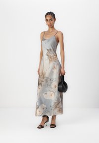 Abito in satin floreale grigio con fiori crema e marroni, caratterizzato da spalline sottili e una silhouette fluida. Abbinato a una borsa nera e scarpe con tacco.