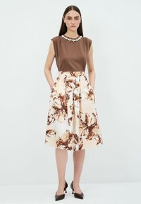 Top marrone con colletto decorativo, abbinato a una gonna crema a lunghezza ginocchio con grandi motivi floreali marroni. Tacchi marroni completano il look.